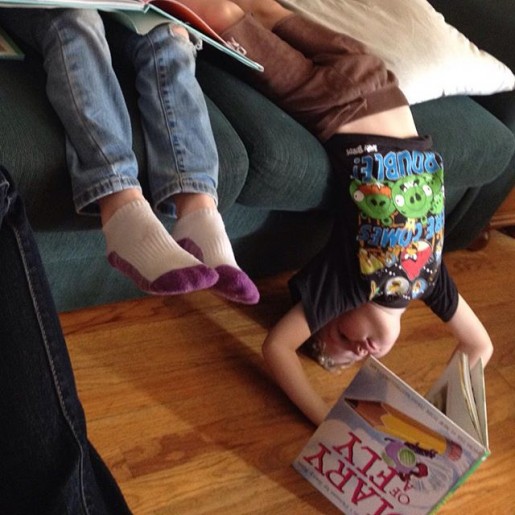 Small child hanging upside down off couch, reading, as one does
