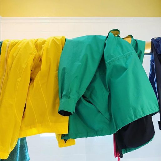 two raincoats, one green, one yellow, drying over a shower door