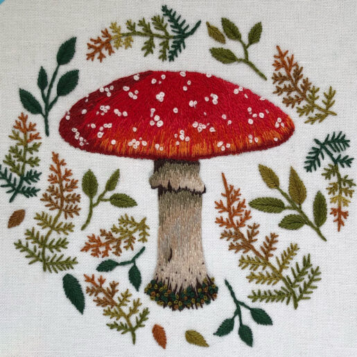 an embroidered mushroom surrounded by autumn leaves