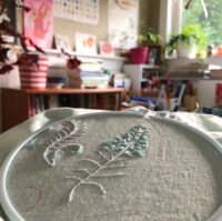 Photo of an embroidery hoop with a fern half stitched