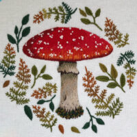 an embroidered mushroom surrounded by autumn leaves