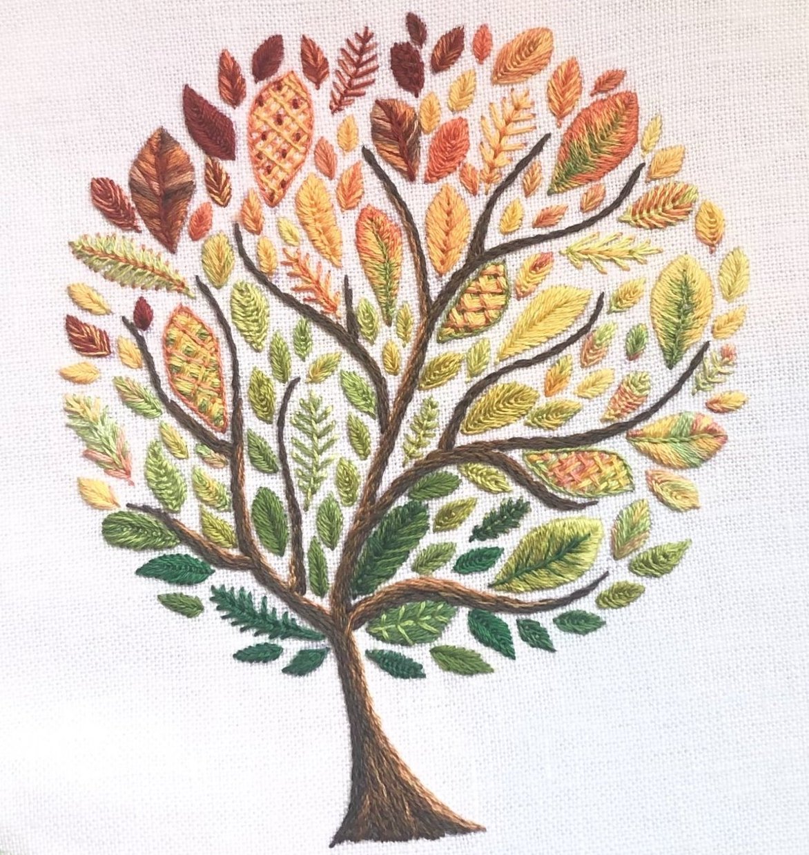 an embroidered tree whose leaves are stitched in a variety of fall colors and different stitches